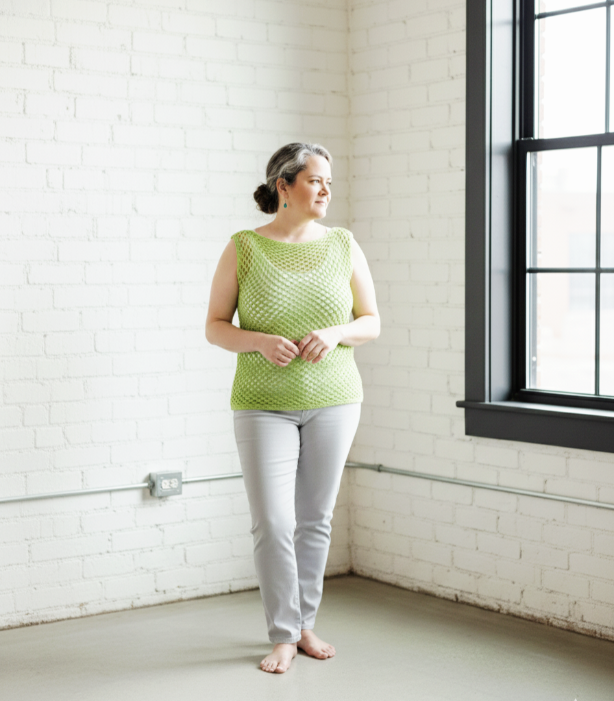 A lime green crochet mesh tank top on a woman in a white loft standing by a large window.