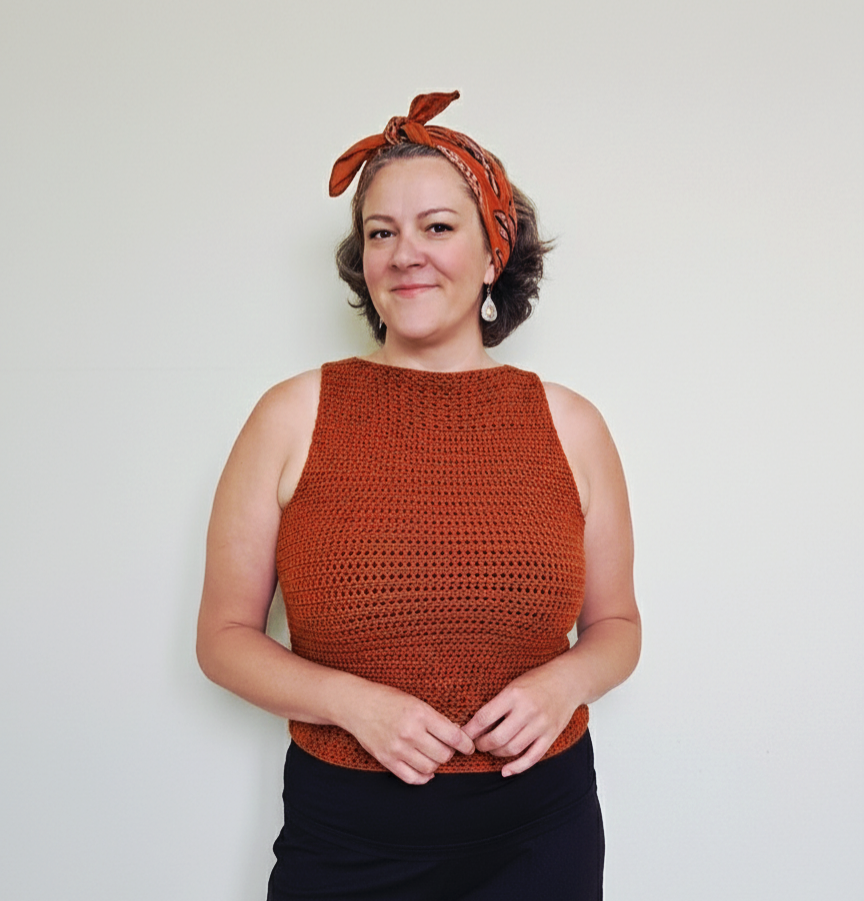 A woman against a white wall waring the sleeveless summer crochet tank top from the pattern provided in the blog for Lulo Stitch Co.