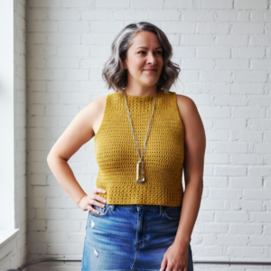 A woman in a modern white loft wearing a mustard yellow sleeveless crochet summer top from the pattern provided.