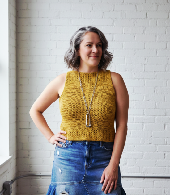 A woman in a modern white loft wearing a mustard yellow sleeveless crochet summer top from the pattern provided.