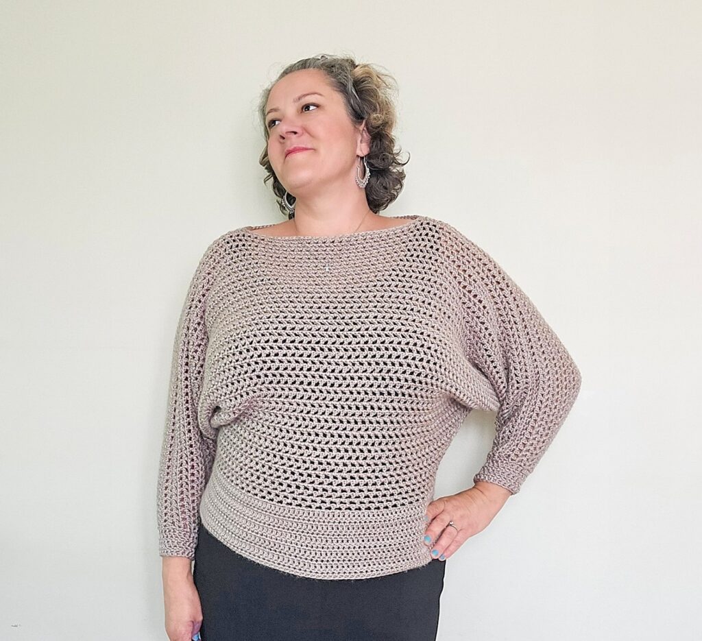 A closeup of a woman in a tan crochet batwing top that is lightweight and versitile.