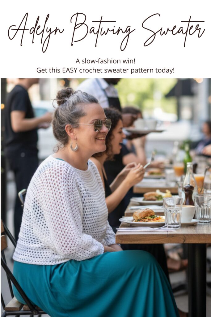 A woman in a white mesh batwing crochet sweater having lunch on an outdoor patio.  She is wearing a teal dress and smiling. 